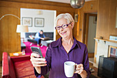 Senior woman using smart phone and drinking tea