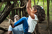 Father watching daughter hang from branch in woods