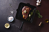 Cooked black angus prime beef ribeye steak on cast iron grilling pan with herbs, butter and spices