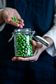 Person in apron standing with glass can of fresh green peas