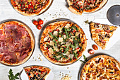 Pizzas with various meat and vegetables on white wooden table