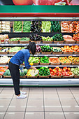 Frau im Supermarkt gibt Paprikaschoten in recycelbaren Beutel