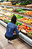 Frau im Supermarkt gibt Paprikaschoten in recycelbaren Beutel