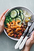 Holding poke bowl with rice and cucumber with beans and mushrooms topped with shrimps