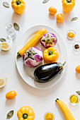 Ripe eggplants and squash in plate placed on table with tomatoes and yellow peppers
