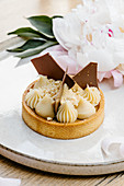 Caramel tart garnished with white and milk chocolate and placed on tray with peony flowers