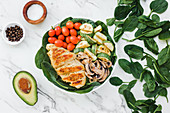 Cherry tomatoes placed inside bowl of roasted chicken and zucchini with mushrooms on spinach leaves