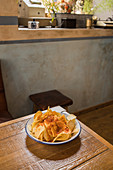 Pile of crispy potato chips in bowl placed on wooden table at home