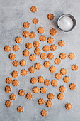 Homemade crusty salted cookies in shape of flowers arranged on gray marble table with pot of salt