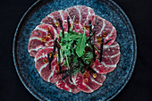 Carpaccio slices on plate garnished with green herbs