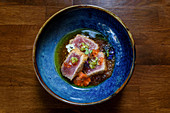 Bowl with seared ahi tuna garnished with caviar and herbs and placed on wooden table