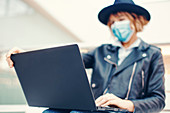 Woman in face mask opening laptop