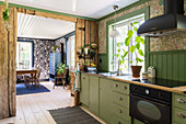 Küchenzeile mit grünen Schrankfronten und rustikale Holzwand zwischen Küche und Esszimmer