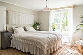 Double bed in bedroom with vintage wallpaper, curtains and frills