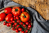 Various types of fresh ripe red tomatoes on wooden tray arranged on rustic wooden table