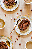 Portions of tasty swiss roll cake placed in plates on wooden table with scattered hazelnuts