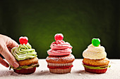 Crop anonymous person taking delicious homemade festive cupcake with green colored whipped cream from table
