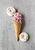 Yummy homemade cherry ice cream in waffle cone placed on table with meringues