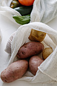 Raw potatoes in eco friendly fabric bags placed on table in kitchen