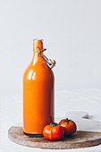 Gazpacho in Bügelflasche mit Tomaten auf Holzbrett