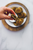 Hand grabbing a lentil falafel from a dish served with yogurt sauce on a wooden table