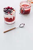 Glass of ice cream with strawberry jam, frozen berries and chocolate chips placed on a wooden white table
