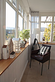 Conservatory with tripod lamp, armchair, and wooden house on the ledge