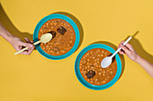 Top view of two hands with Callos dishes over yellow background