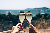 Crop anonymous couple enjoying summer holidays and cheering with glasses of champagne while spending sunny day at seaside