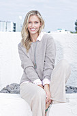 A young blonde woman on the beach wearing a light jumper and trousers