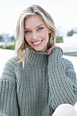 A young blonde woman on the beach wearing a grey knitted jumper