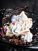 Dessert made from meringue cookies decorated with violet flower and placed on plate with cream and chocolate