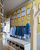 Letters and certificates above school uniforms hung from wall hooks and storage bench in hall