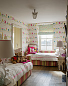 Twin beds with striped frames in children's bedroom with bird-patterned wallpaper