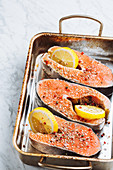 Fresh salmon steaks with aromatic seasoning and lemon slices on metal baking sheet