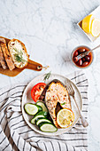 Grilled salmon steak with lemon and herbs served with fresh sliced cucumber and tomato