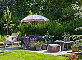 Terrace with outdoor furniture, flowers and sunshade in summer garden