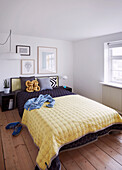 Double bed with bedspread in bright bedroom with wooden floorboards