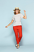 A blonde woman wearing a straw hat, a light top and red trousers