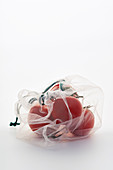 Tomatoes in net mesh bag on white background