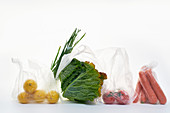 Still life with food in plastic bags on white background