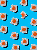 Sweet candies in shape of fried eggs with one bitten arranged on blue background