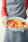 A woman holding a raspberry and peach crumble topped with oat crumbles