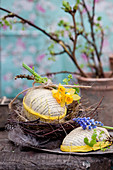 Handmade cardboard Easter eggs in nest of twigs with narcissus and grape hyacinth flowers