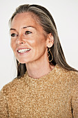 A woman with salt-and-pepper hair wearing earrings and a shimmery golden jumper