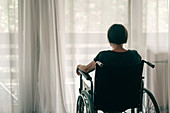 Depressed woman in wheelchair looking out the window