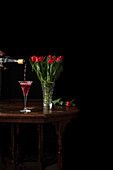 Pouring sparkling wine in glass, bouquet of red tulips