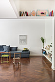 Gray upholstered sofa in a white living room with bookcase and high ceilings