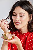 A young brunette woman wearing a red-and-white polka dot top applying make-up with a brush