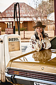 A grey-haired woman leaning against a classic car